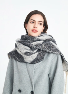 Close-up of thick knit tassel scarf with black and white argyle pattern on wool coat