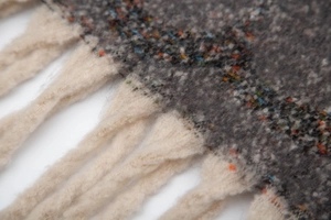 Macro detail of dark grey jacquard scarf featuring colorful dots and cream-white twisted tassels