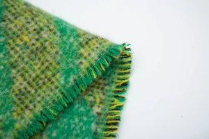Dettaglio di sciarpa scozzese verde in mohair con trama a maglia spessa e frange
