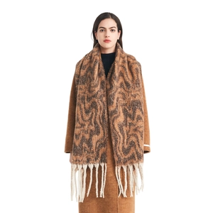 Brown knit scarf with wavy jacquard pattern and chunky white tassels on wool coat