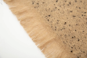 Detail of beige jacquard knit scarf with black specks and fringe trim texture