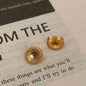 Macro shot of gold sunburst textured earring backs on vintage book pages backdrop