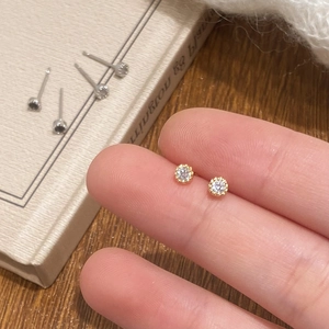 Minimalist round cubic zirconia stud earrings with gold base shown on fingertips
