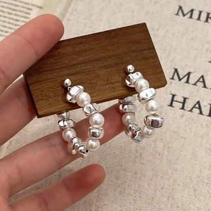 Detail view of irregular silver metal beads and white pearls on hoop earrings