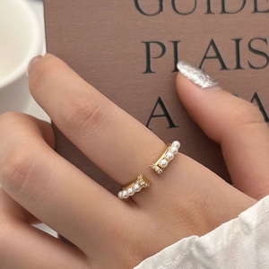 Gros plan d'une bague dorée réglable avec perles et zircons portée à l'index droit
