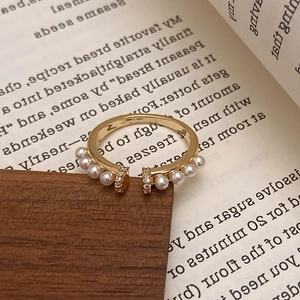 Bague vintage dorée avec perles et zircons présentée sur bois sombre et livre