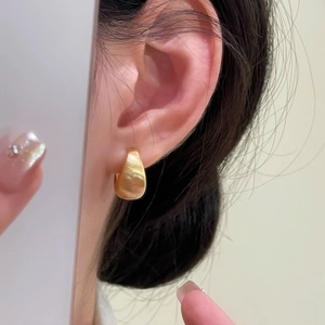 Close-up of polished gold teardrop earrings showing smooth metallic texture on ear