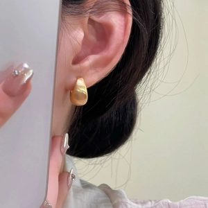 Close-up of elegant matte gold water drop earrings worn by a model in a soft setting