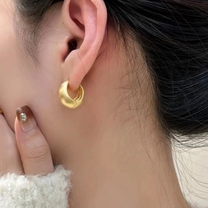 Close-up of matte gold chunky hoop earrings with brushed texture on a female model