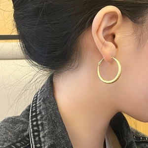 Detailed view of large gold hoop earrings with hammered metal texture on model