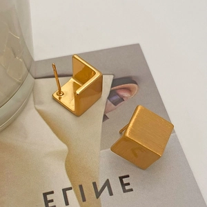 Detailed shot of gold geometric earrings with brushed and polished cube finish on a magazine