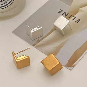 Macro detail of geometric cube earrings with matte brushed gold and silver finish