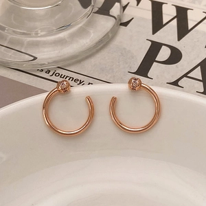 Detail of rose gold C-shaped earrings with micro-pave diamond spheres on a white bowl