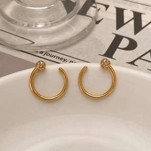 Detailed close-up of gold C-shaped earrings with zircon-inlaid spheres on white ceramic