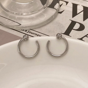 Macro detail of silver C-shaped earrings with pavé-set crystal beads on white ceramic