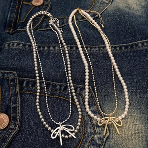 Doppellagige Perlenhalskette mit Schleifenanhänger in Silber und Gold auf Denim