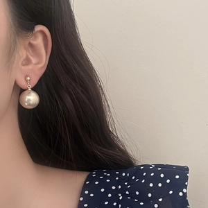 Close-up of large champagne pearl drop earrings on model with gold stud detail
