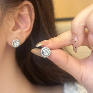 Detail of round halo stud earrings with cubic zirconia inlay on model's ear and fingers
