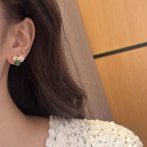 Gros plan de boucles d'oreilles nœud avec zircons brillants et perle en calcédoine vert foncé