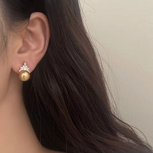 Detailed close-up of golden pearl earring with crown-shaped zircon setting on ear