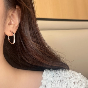 Close-up of a silver geometric square hoop earring worn on a female ear with a minimalist look