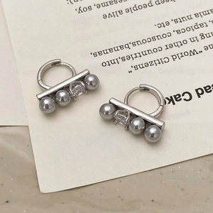 Macro view of silver-tone earrings with grey pearls and clear zircon gemstones on card