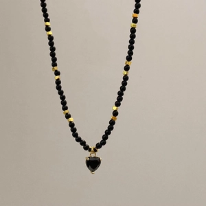 Gros plan sur le collier en perles noires fait main avec un pendentif cœur doré