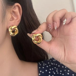 Close-up of golden triple twisted knot earrings worn by model for elegant style