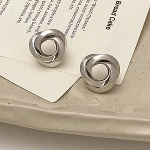 Macro detail of silver intertwined multi-layer hoop earrings on a ceramic dish