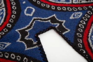 Macro detail of red ethnic jacquard shawl with bohemian star patterns and overlock stitching