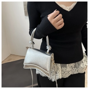 Detail of silver crocodile-embossed crossbody bag with hourglass base and knotted handle