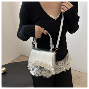 Detailed view of silver crocodile pattern handbag with unique curved base and knot handle