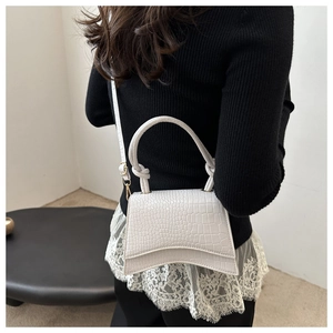 Close-up of small faux crocodile handbag with curved base and adjustable strap detail