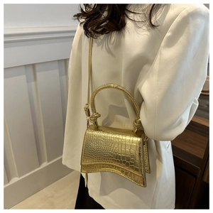 Detail of gold crocodile embossed crossbody bag with curved base and shiny metallic finish