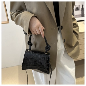 Detailed view of black crocodile pattern handbag with knot handle and curved base design