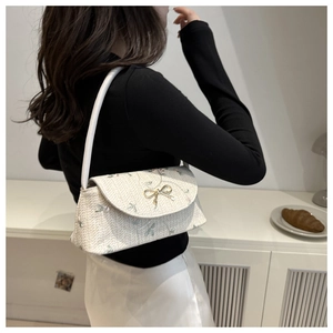 Detail of floral embroidery and gold bow buckle on straw shoulder bag worn by model