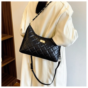 Classic black quilted shoulder bag with gold chain strap shown on beige trench coat