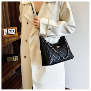 Detail view of black quilted leather shoulder bag with gold chain and buckle on a model