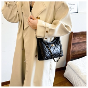 Quilted black chain shoulder bag shown on model wearing a classic beige trench coat