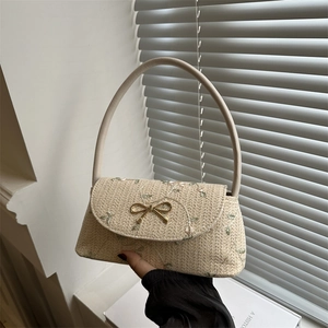 Straw shoulder bag with floral embroidery and golden bow clasp held by a model