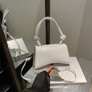 White crocodile pattern shoulder bag with braided handle and curved base in a hand-held view