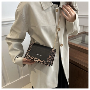 Detail of crossbody bag with leopard print edges and gold chain strap on a trench coat