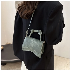 Detail of green hourglass crossbody bag with knot handle worn over a black blazer