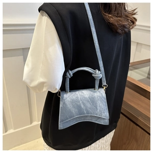 Rear view of a blue denim texture small handbag with curved base and knotted handle strap