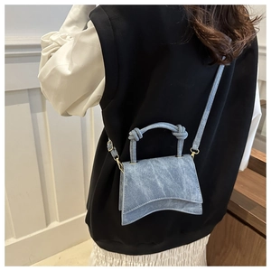 Detail of grey-blue denim mini bag with braided rope handle and wavy bottom worn by a model