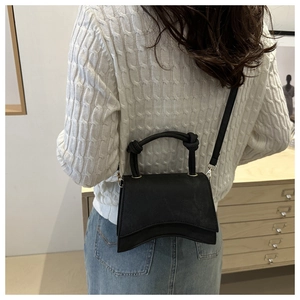 Close-up of black crossbody bag with wave design and knot handle on a white sweater