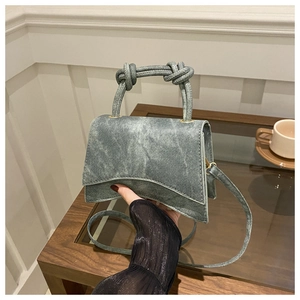 Detail of structured denim trapezoid handbag with knotted handles and slender strap