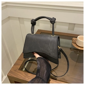 Detail of black crossbody bag with knotted handle and matte leather finish on a wooden table