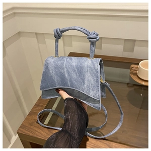 Detail of light blue denim crossbody bag with unique asymmetric shape and knotted handle