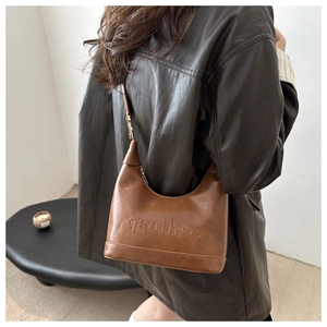 Close-up of brown matte leather hobo bag with embossed lettering and slim shoulder strap